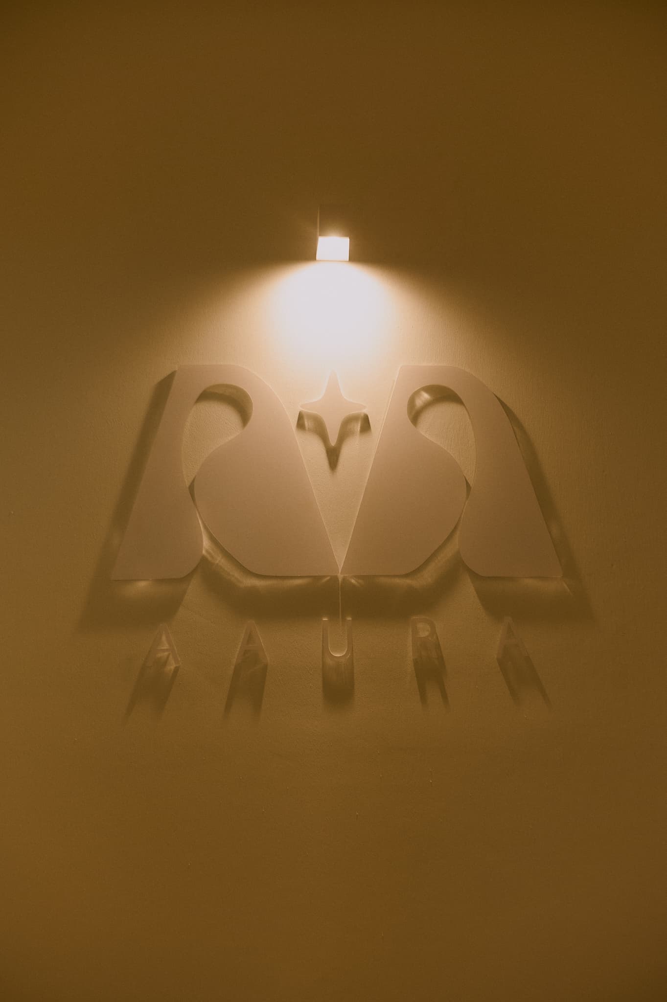 Logo de AAURA en relieve sobre pared del estudio con iluminación cálida